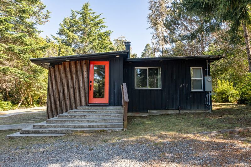 The Black Cabin's dark exterior and red front door among the trees in Fort Bragg, California